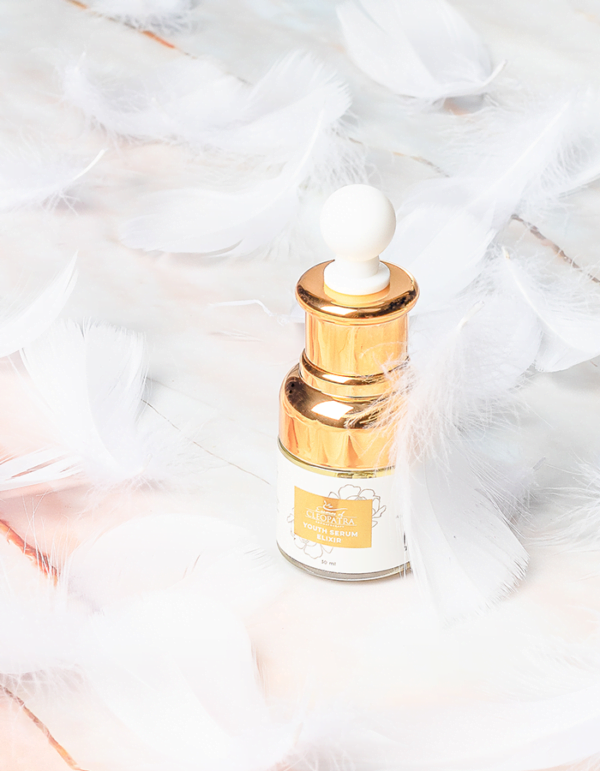 a bottle of YOUTH SERUM ELIXIR with white feathers on a marble table.